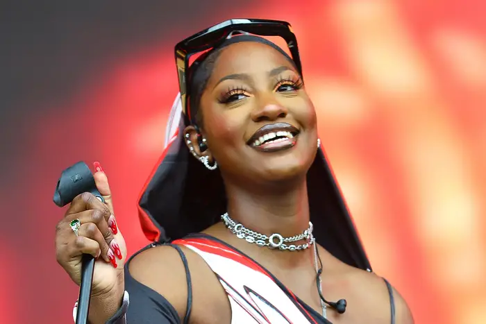Tems performing live, smiling, microphone in hand